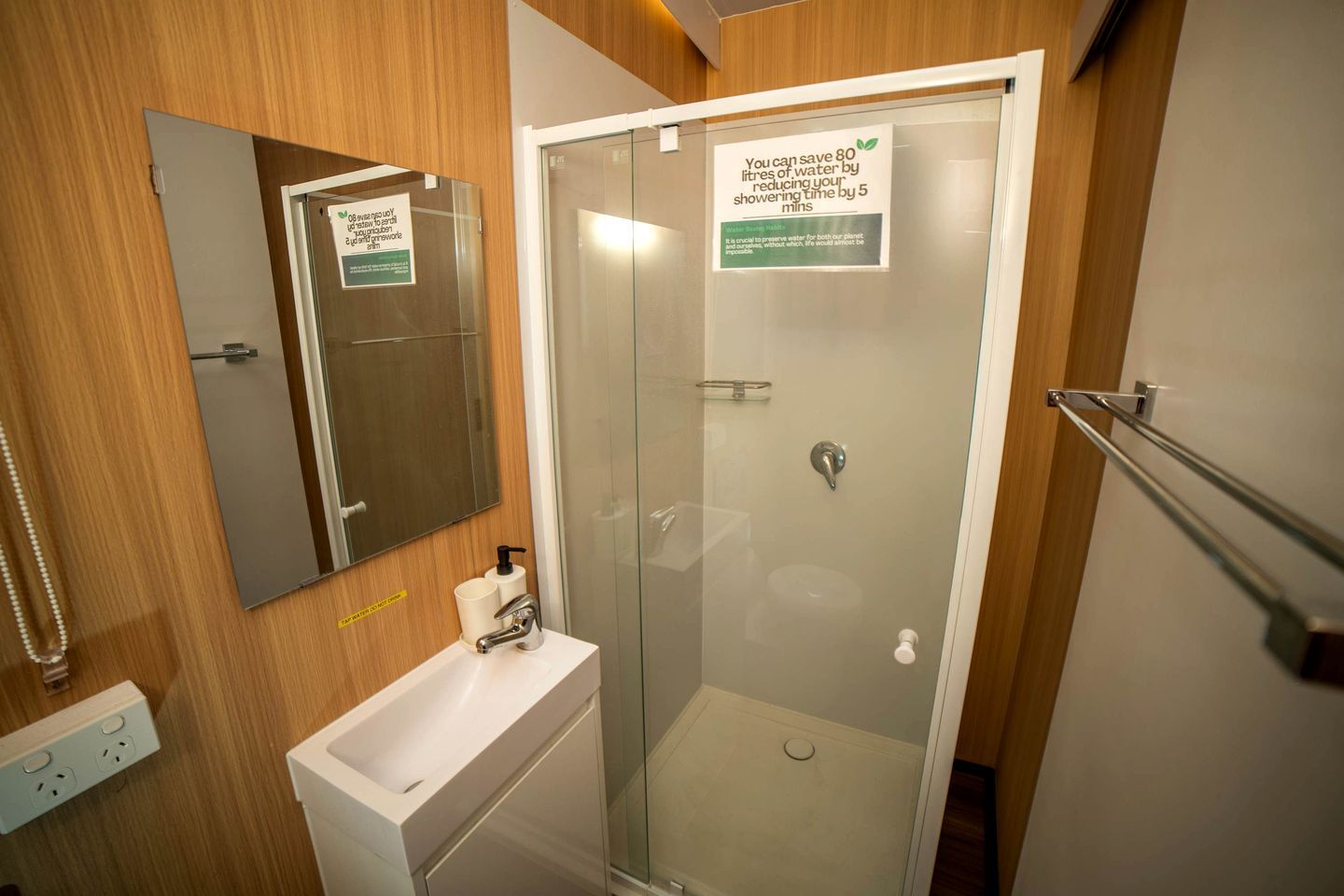 Een moderne badkamer met een glazen douchecabine, een wit wastafeltje en een spiegel.
