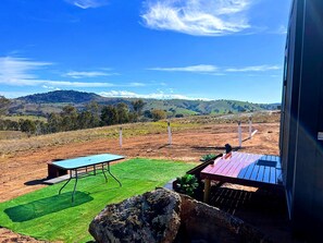 A patio with a table and chairs, a rock, and a view of hills in the distance.
