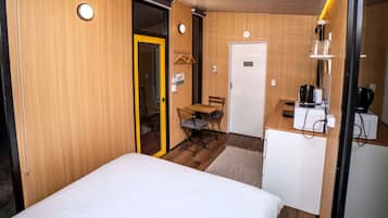 A compact room with a bed, a small dining table with chairs, a kitchenette with a microwave, and a door leading to a bathroom.
