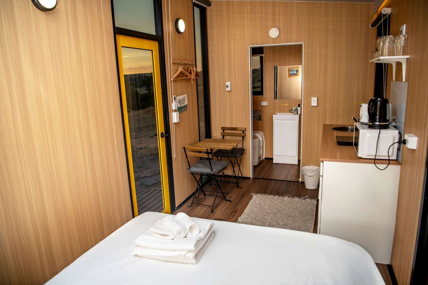 Een compacte hotelkamer met een bed, een klein tafeltje, een kitchenette en een badkamer.