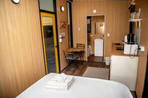 Une chambre d’hôtel de taille réduite, comprenant un lit, une petite table, une kitchenette et une salle de bain.
