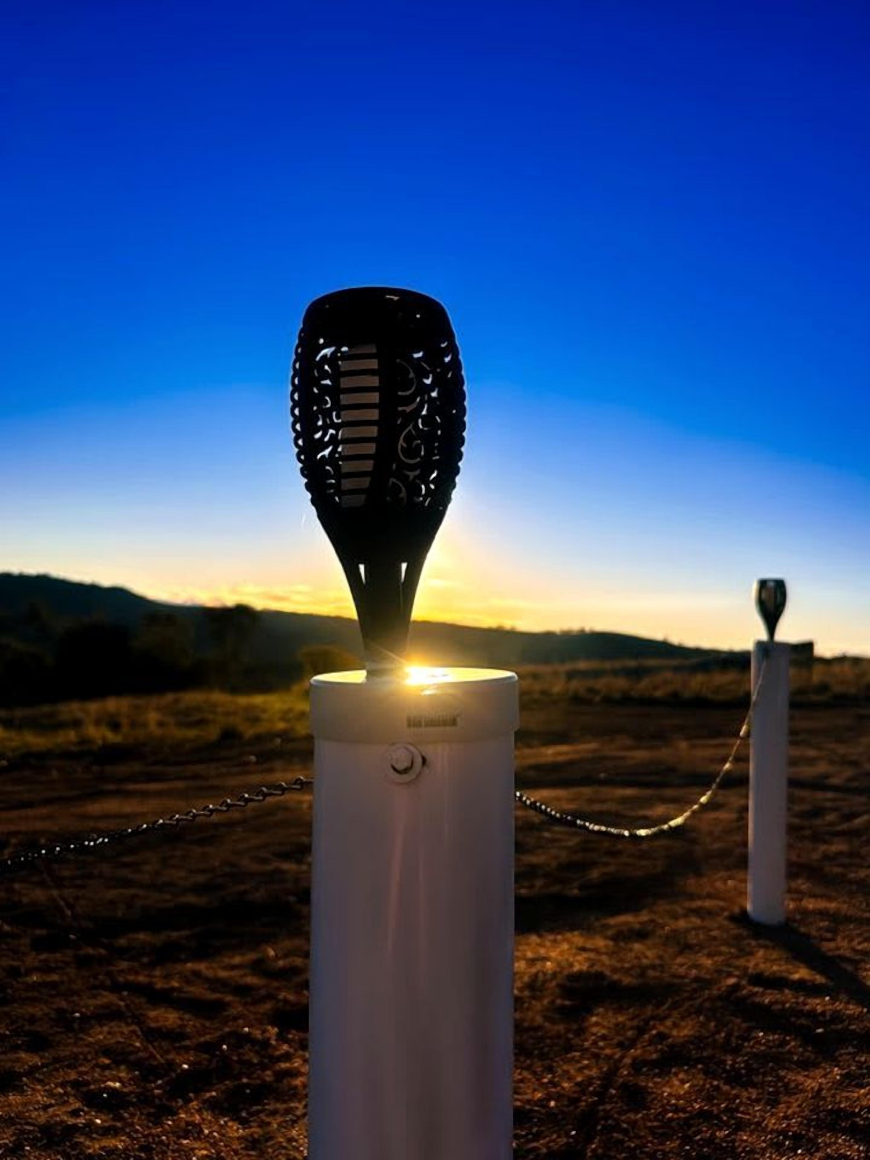 A microphone on a stand with a chain, set against a sunset background.