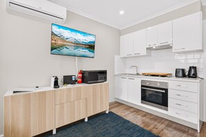 A modern kitchen with white cabinets, a built-in oven, and a flat-screen TV mounted above the counter. - Peaceful 1-Bed Near Canberra Hospital (Hughes)