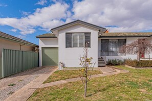 A single-story house with a green garage door, a small front yard with a young tree, and a clear sky. - Peaceful 1-Bed Near Canberra Hospital (Hughes)