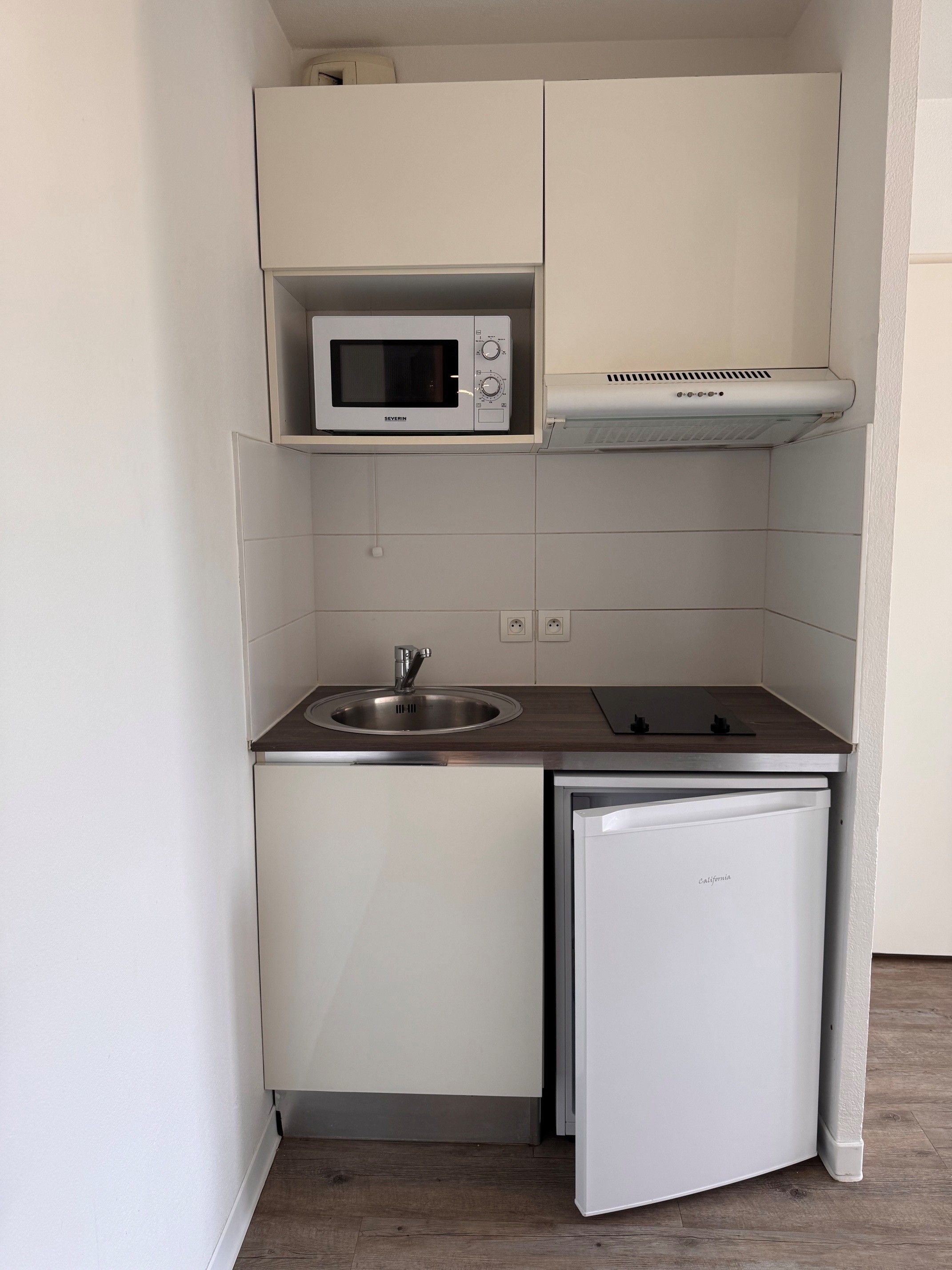 A compact kitchenette with a microwave, sink, and a small refrigerator.