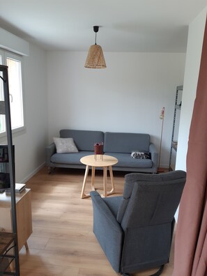 A living room with a grey sofa, a round wooden table, and a grey armchair. - Spacious, fully equipped house surrounded by greenery, with a pool and a wood stove—perfect for families! (Cestas)