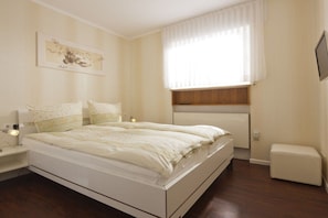 A bedroom with a bed, bedside table, lamp, and a window with curtains. - Holiday apartment in Norderney with Wi-Fi (Norderney)