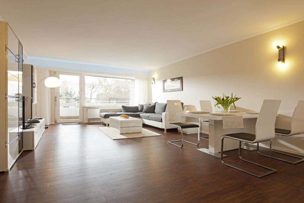 Ein modernes Wohnzimmer mit einer Couch, einem Esstisch und Stühlen. Ein Fenster lässt natürliches Licht herein und bietet einen Ausblick.
