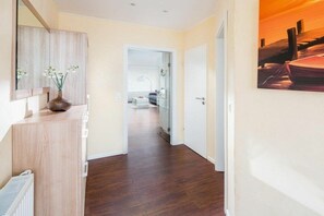 A hallway with a wooden floor, a white radiator, a mirror, and a painting on the wall. - Holiday apartment in Norderney with Wi-Fi (Norderney)