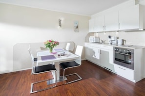 A modern kitchen with white cabinetry, a built-in oven, and a dining area with a white table and chairs. - Holiday apartment in Norderney with Wi-Fi (Norderney)