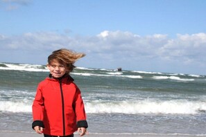 Eine Person steht am Strand, im Hintergrund sind Wellen zu sehen.