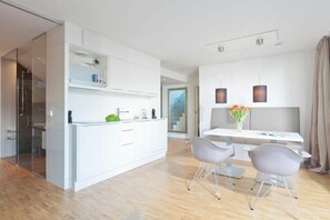 Eine moderne Küche mit weißen Schränken, ein Essbereich mit weißem Tisch und zwei Stühlen sowie Pendelleuchten über dem Tisch.