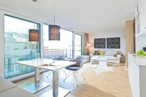 A modern living room with a dining area, large windows, and a view of the outdoors. - Schippers Huus Apt. 6 (Norderney)