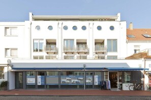A white building with a flat roof, multiple balconies, and a storefront with glass doors. - Schippers Huus Apt. 6 (Norderney)