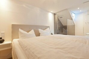 A modern hotel room with a large bed, a bedside table, and a glass-enclosed shower area. - Schippers Huus Apt. 6 (Norderney)