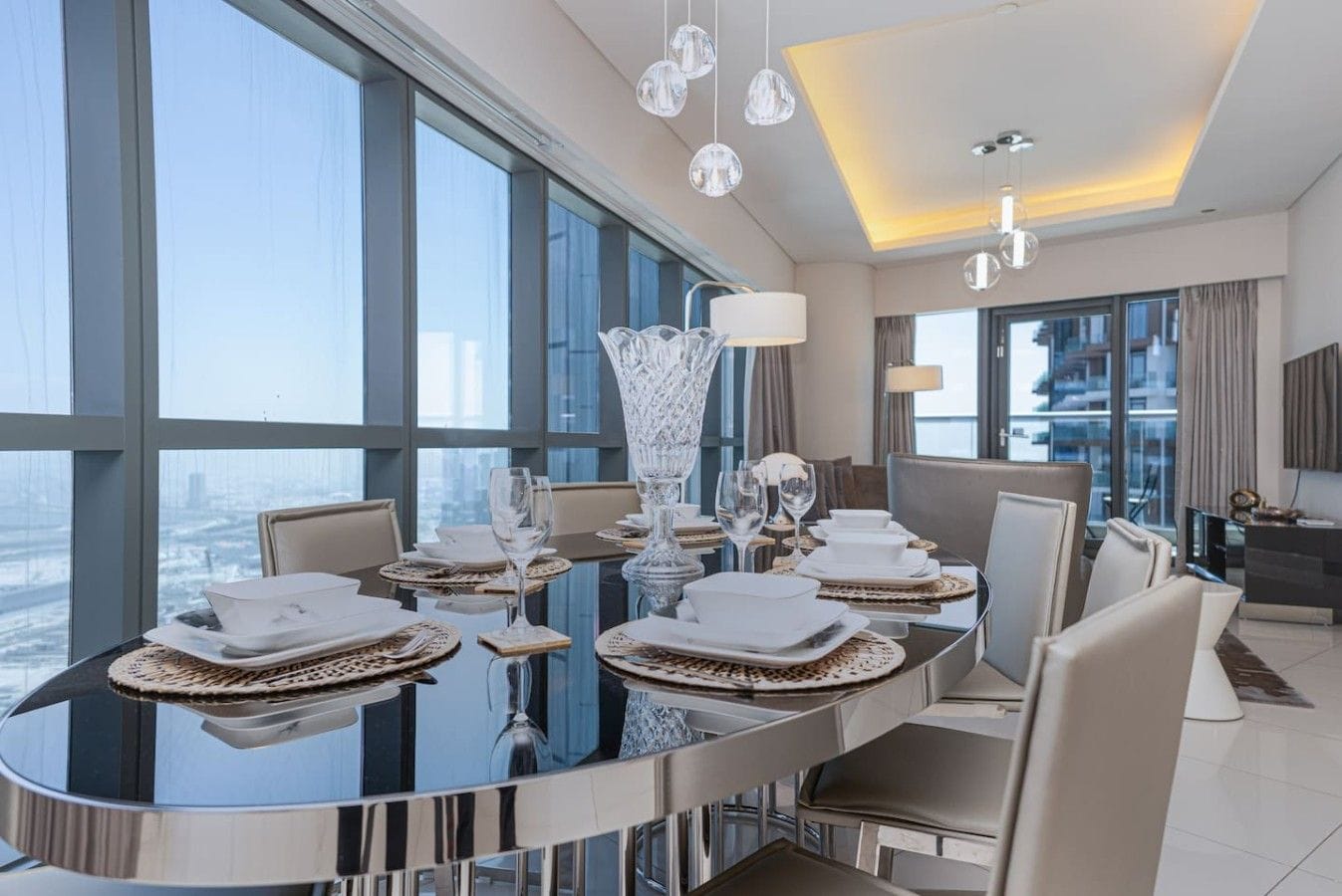 Ein moderner Essbereich mit einem großen runden Tisch, der für eine Mahlzeit gedeckt ist, großen Fenstern mit Blick auf die Stadt und zeitgemäßen Leuchten.