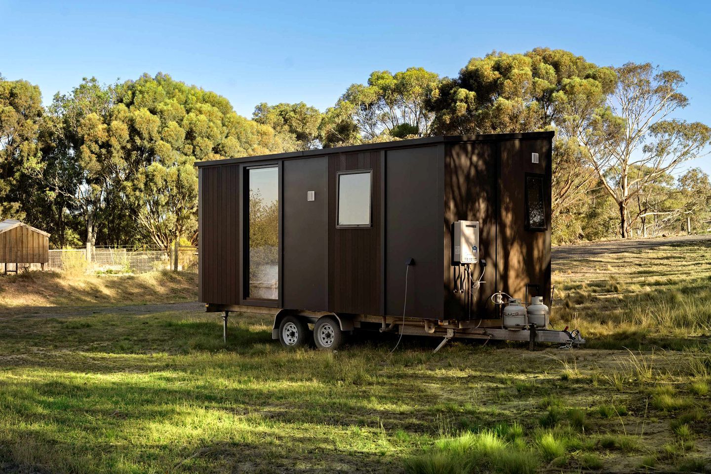 Una casa móvil pequeña y oscura con puerta corrediza, calentador de agua y tanques de propano sobre un remolque.
