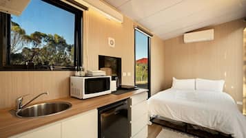 Un dormitorio moderno con cama, microondas integrado y ventana con vista a árboles.