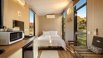 Habitación compacta con cama, microondas, lavamanos y ventana con vistas a zonas verdes.