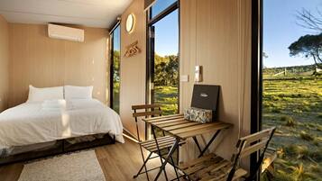 A modern bedroom with a large bed, a wooden desk, and a view of a grassy field.