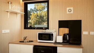 A compact kitchen with a microwave, toaster, and coffee maker on the countertop, a sink, and a window with a view of trees.