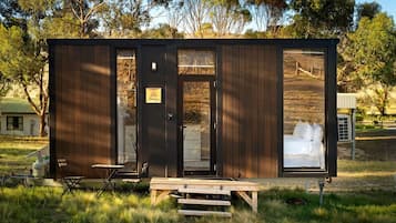 Una cabaña pequeña de una sola habitación, con una puerta, una ventana y una banca afuera.