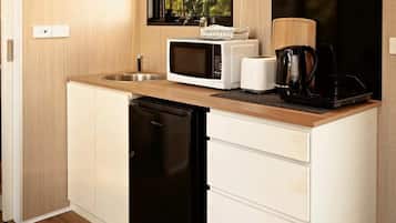 A compact kitchen with a microwave, toaster, and coffee maker on the counter, a dishwasher, and a window with a view of trees.