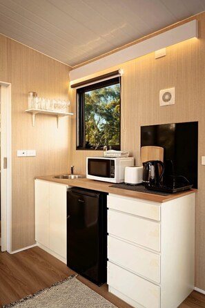 A compact kitchen with a microwave, toaster, and coffee maker on the counter, a dishwasher, and a window with a view of trees.