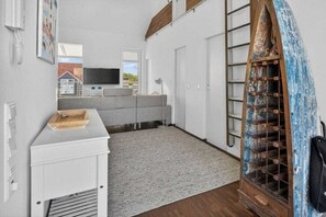 Ein modernes Wohnzimmer mit einem grauen Sofa, einem kleinen weißen Schrank, einer Holzleiter und einem Fernseher an einer weißen Wand.