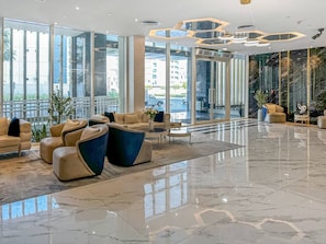 Eine großzügige Lobby mit modernem Design, ausgestattet mit einer Sitzecke mit Sofas und Sesseln, einer Glaswand mit Ausblick nach draußen und einem polierten Marmorboden.