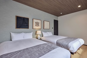 Quarto de hotel com duas camas, uma mesa de cabeceira com abajur e três obras de arte emolduradas na parede.