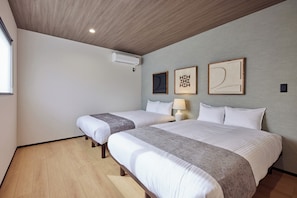 A hotel room with two beds, a ceiling fan, an air conditioning unit, and artwork on the wall.