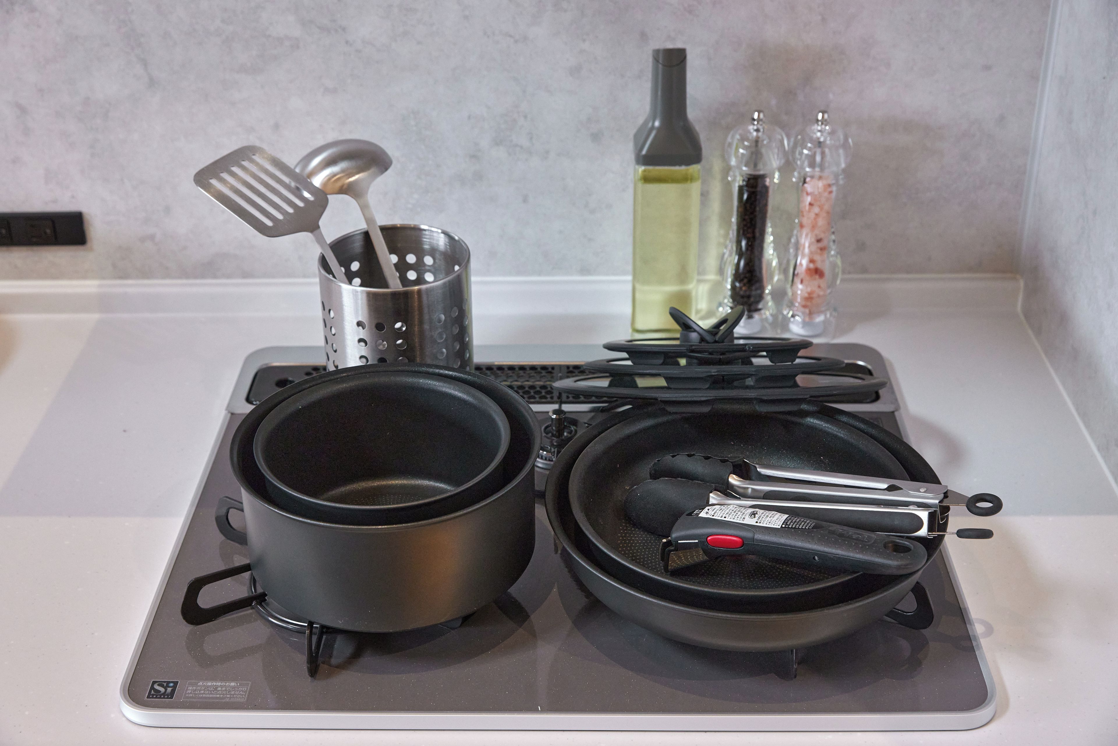 A kitchen with two pots, a colander, a bottle, and a pan on a stove.
