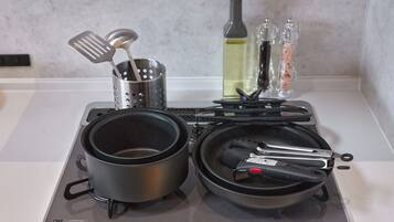 A kitchen with two pots, a colander, a bottle, and a pan on a stove.