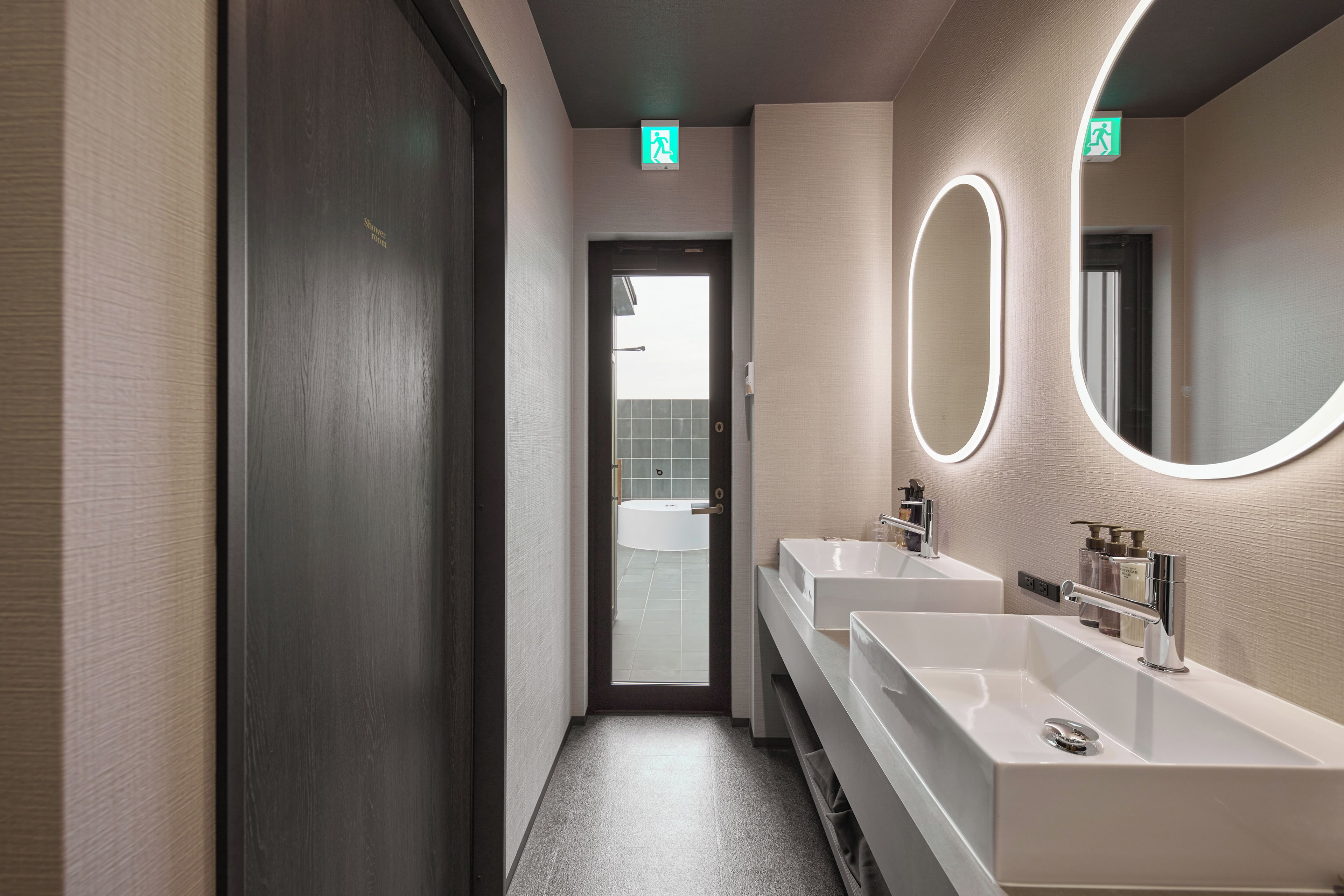 Un baño moderno con dos lavamanos, un espejo grande y una puerta que da acceso a la zona de ducha.