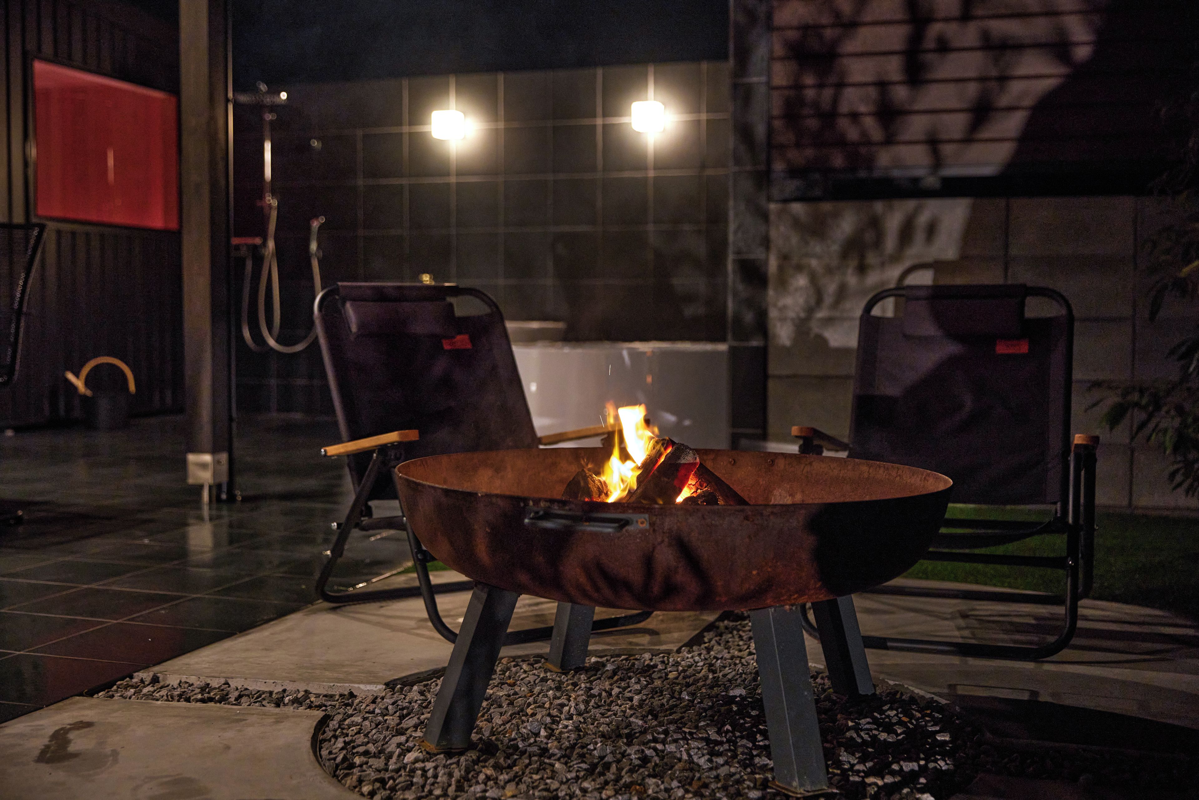 An outdoor seating area with a metal fire pit in the center, surrounded by two chairs.