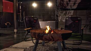 An outdoor seating area with a metal fire pit in the center, surrounded by two chairs.