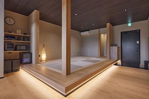 A room with a wooden floor, a bed with a wooden frame, a wall-mounted clock, and a shelf with various items.