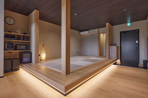 A room with a wooden floor, a bed with a wooden frame, a wall-mounted clock, and a shelf with various items.