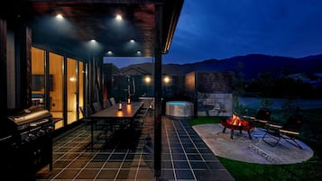 An outdoor patio with a dining table, chairs, a grill, and a hot tub.