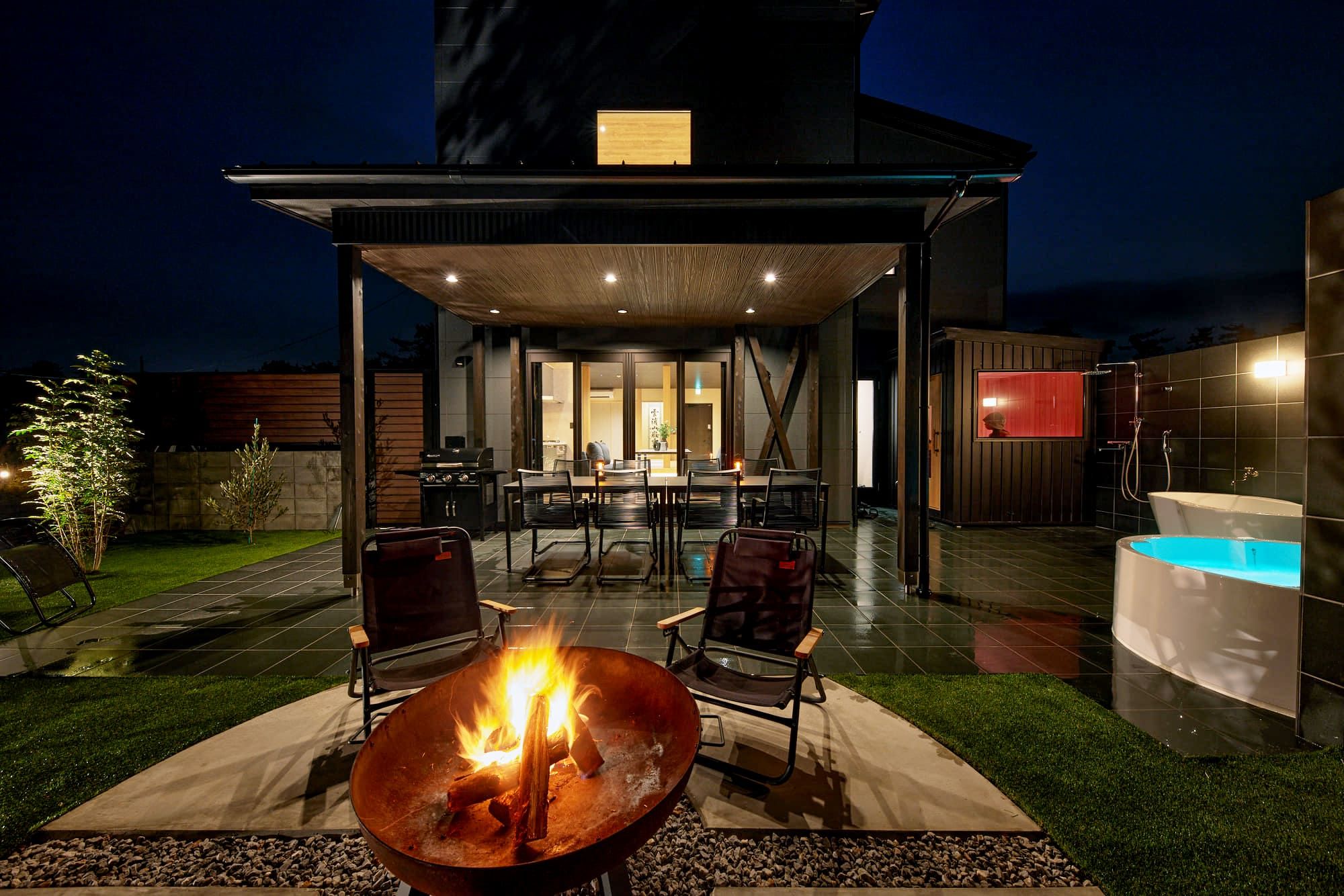 En udendørs patio med bålsted, siddepladser, en pool og et overdækket spiseområde.