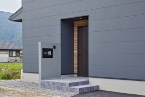 A modern building with a grey facade, a wooden door, and a small set of steps leading to the entrance. - SUITE VILLA -SHOU- (Takashima-shi,)