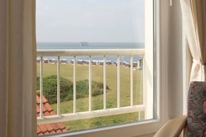 Quarto com janela vista para uma praia com guarda-sóis e um navio ao longe.