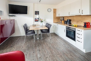 A modern kitchen with a dining table, chairs, a TV mounted on the wall, and a clock. - Holiday apartment in Norderney with Wi-Fi (Norderney)