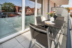 Ein Balkon mit Tisch und Stühlen, einer Blumenvase und Blick auf Gebäude.