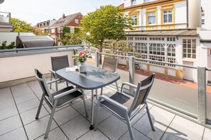 A balcony with a table and chairs, a grill, and a view of a building with yellow trim. - Holiday apartment in Norderney with Wi-Fi (Norderney)