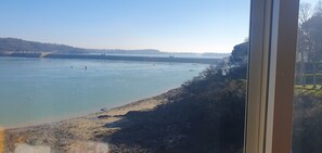 A view of a river with a sandy beach and rocky shoreline, a bridge in the distance, and trees along the riverbank. - Route du Rhum with a Sea View in Dinard (Dinard)