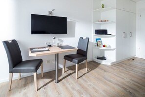 A modern room with a flat-screen TV mounted on the wall, a wooden desk with a chair, and a white shelving unit with various items. - Holiday apartment in Norderney with sauna (Norderney)
