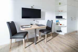 A modern room with a flat-screen TV mounted on the wall, a wooden desk with two chairs, and a white shelving unit with various items. - Holiday apartment in Norderney with sauna (Norderney)