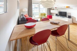 A modern living room with a dining area, a television, and a window with a view. - Holiday apartment in Norderney with Wi-Fi (Norderney)